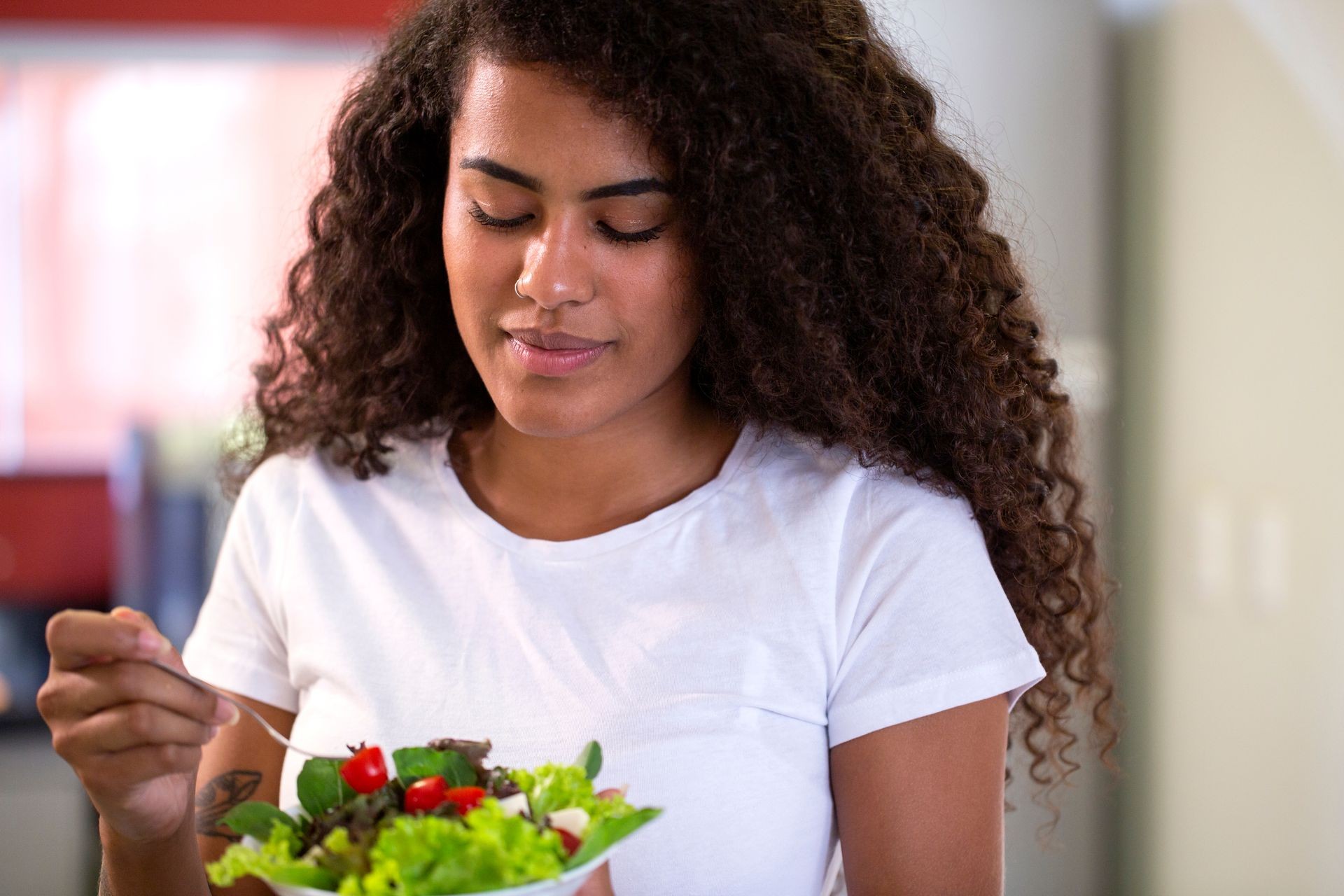 cheerful young afro american woman eating vegetable salad in home kitchen.